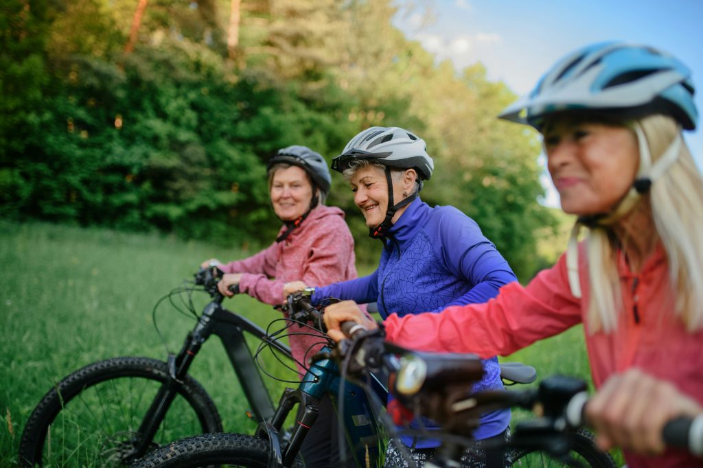 happy active senior women friends pushing bicycles together outdoors in the nature